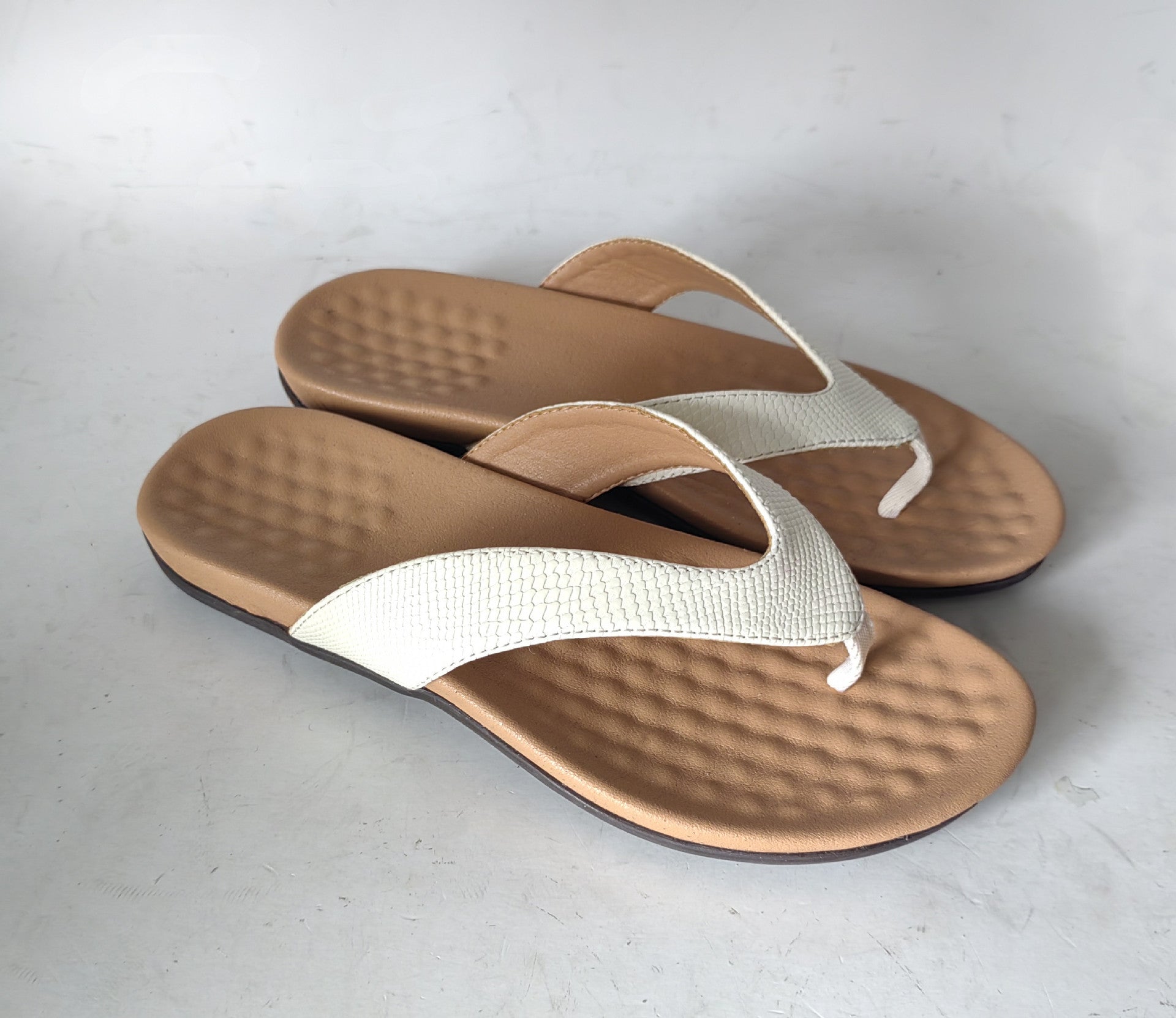 Women’s flat heel thong sandals in white PU leather with rubber sole for casual summer wear.