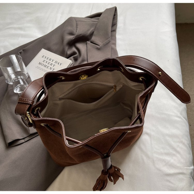 Brown bucket bag with tassel detail and open interior compartment on bed.