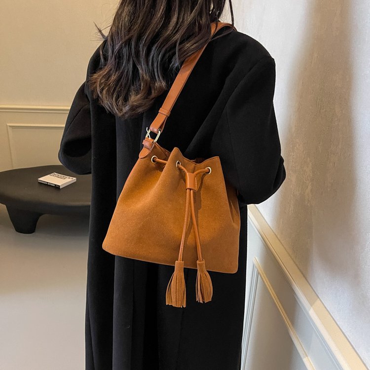 Bucket bag with tassel detail in brown PU leather, featuring a drawstring and single shoulder strap.