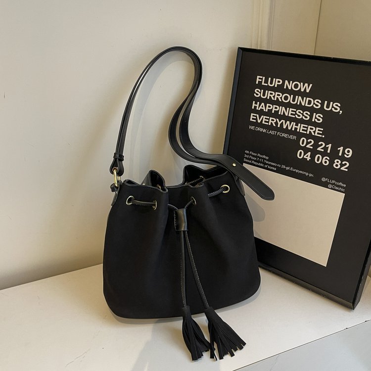 Stylish bucket bag with tassel detail in black PU leather featuring a drawstring closure and single shoulder strap.