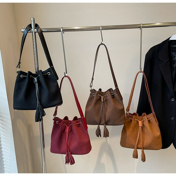 Bucket bag with tassel in four colors hanging on a rack.