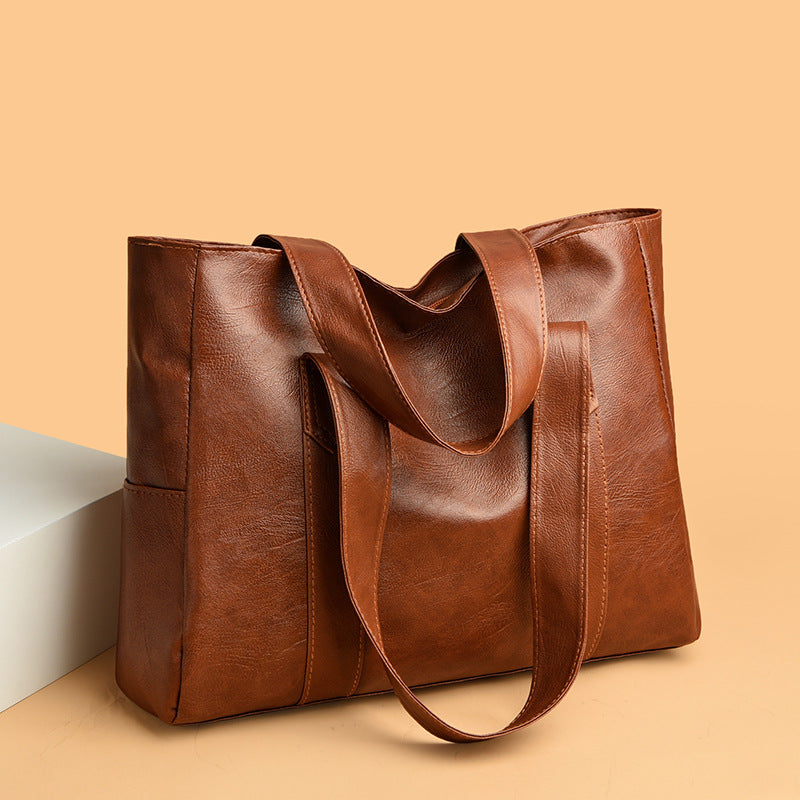 Versatile large capacity brown PU leather tote bag on beige background.