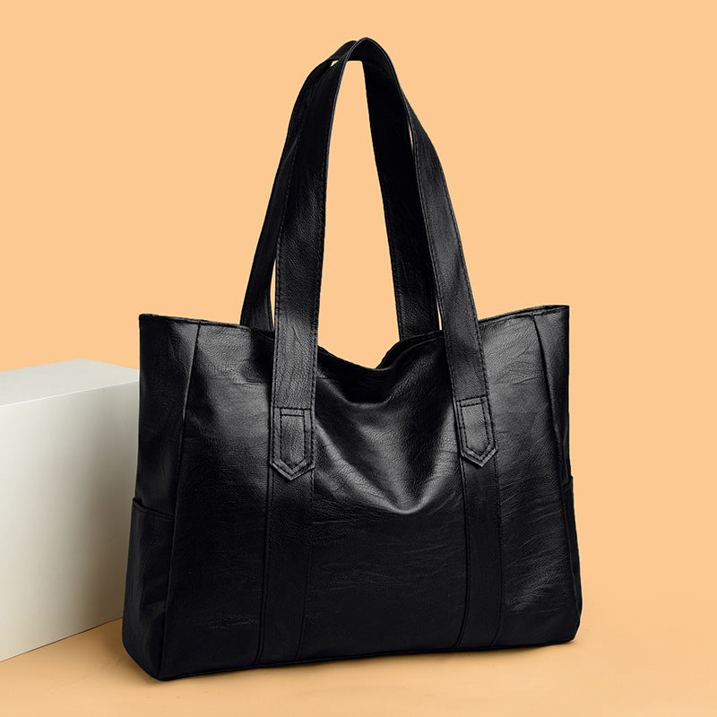 Large capacity black tote bag made of PU leather on a beige background.