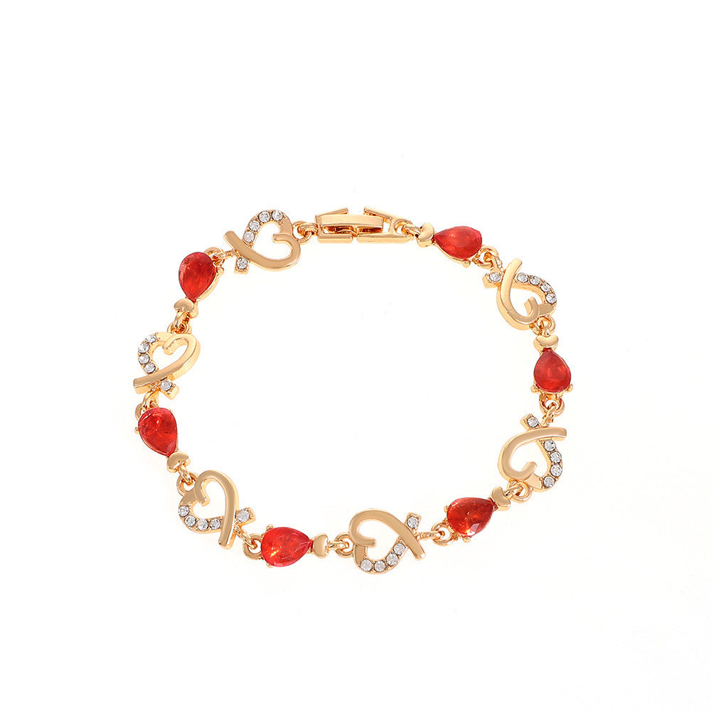 Heart-shaped bracelet with red stones and rhinestones on a gold chain.