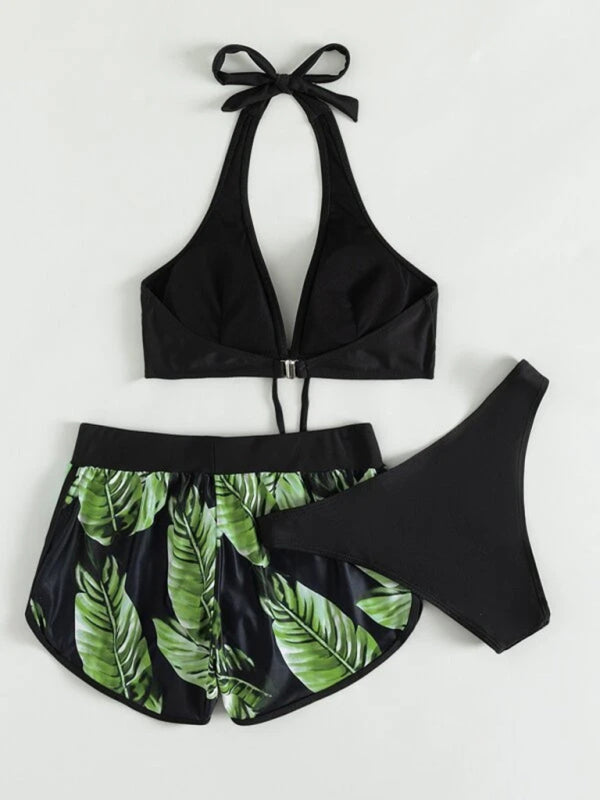 Women's tropical print halter neck bikini set, three-piece with top, bottoms, and leaf-patterned swim shorts.