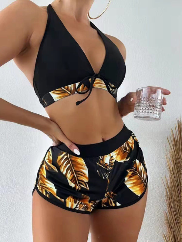 Women’s tropical print halter neck bikini three-piece set with black top and vibrant leaf-printed shorts.