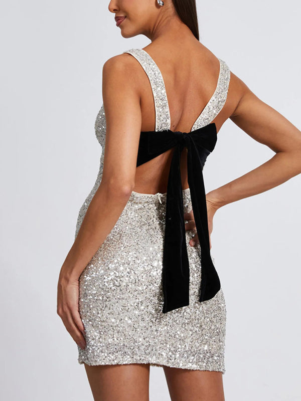 Backless and sleeveless fitted silver sequin dress with open back and black bow detail.